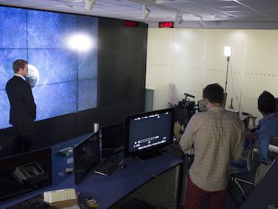 A still from a video shoot for Oxford Space Systems, a group of people are filming a man in front of a wall of video panels